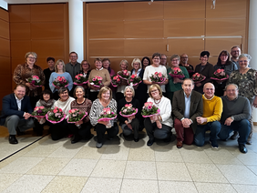 Die Gruppe vor einer Holzwand, erste Reihe in Hocke, mit bunten Blumensträußen
