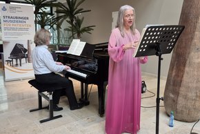 (©Ursel Urban) Auf dem Bild sind die Sopranistin Brigitte Thoma und der Pianist Wolfgang Kraus zu sehen, die gemeinsam ein Konzert im Klinikum geben. Thoma steht singend neben dem Flügel, während Kraus sie am Klavier begleitet.