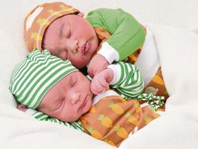 Zwei Babys aneinandergekuschelt schlafend mit mützchen und Bodies und Pullis in grün, weiß, braun, zum Teil gestreift und mit karotten bemustert.