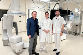 Überregionale Stroke Unit - TEMPiS Netzwerk (© Sandra Wimmer) Der Geschäftsführer in dunkelblauem Sacko, schwarzem Hemd und Schuhen und grauer Hose neben den beiden Ärzten in weiß vor der futuristisch anmutenden Anlage