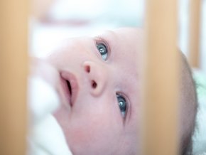 Geburtshilfe Straubing (© Johannes Lehner) Im Vordergrund Nahaufnahme eines Babgesichts im Zustellbett, dahinter unscharf die Mutter ihm zugewandt