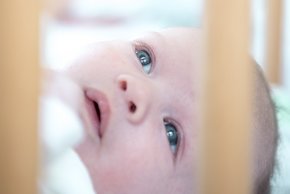 Geburtshilfe Straubing (© Johannes Lehner) Im Vordergrund Nahaufnahme eines Babgesichts im Zustellbett, dahinter unscharf die Mutter ihm zugewandt