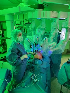 Ärztin in OP-Montur neben dem DaVinci und Patienten stehend, auf den Monitor schauend, grünes Licht