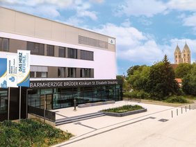 Das Klinikumsgebäude mit den Fahnen im neuen Corporate Design - im Log mit orangfarbenen Bögen neben blauem Granatapfel