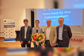 Hämatologieforum Referenten (© Daniela Müller) Die Dame mit Blumenstrauß, alle Brille und Sacko vor einer Präsentation