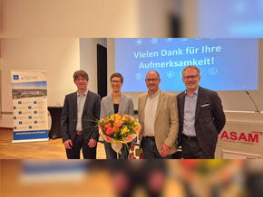 Die Dame mit Blumenstrauß, alle Brille und Sacko vor einer Präsentation