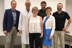 Perinatalkonferenz (© Sandra Pfaffinger) Dr. Scholz ist in weißem Kittel, alle anderen in zivil, freundlich lachend vor einer Leinwand