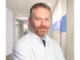 Prof. Dr. Jochen Grassinger (© Johannes Lehner) Portrait von Arzt mit Bart, rothaarig-grau meliert, lächelnd in Kittel, Hemd und Krawatte