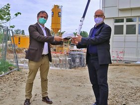 Bild von Klinikums-Geschäftsführer Dr. Christoph Scheu, wie er den von Ministerpräsidenten Dr. Markus Söder signierten Bauhelm dem neuen Eigentümer Erwin Hausmann übergibt.