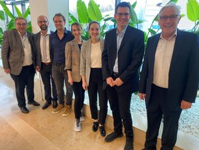 Zweiter Niederbayerischer Hörtag (© Ursula Eisenmann) Ein Teamfoto mit links drei und rechts zwei Männern, in der Mitte zwei Frauen, stehende und lächelnd vor Grünpflanzen und einer Säule im Foyer des Klinikums. Sie sind elegant gekleidet.